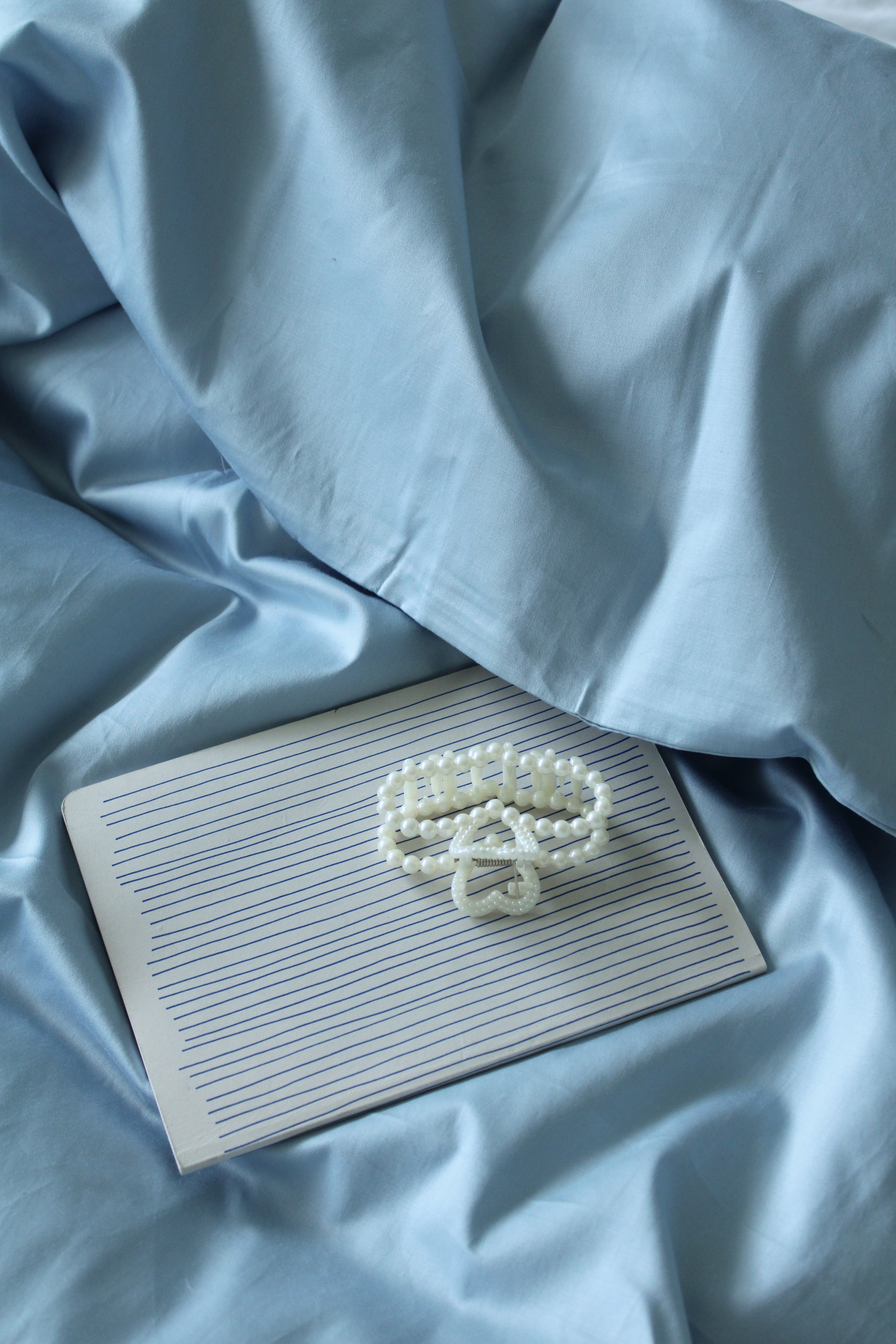 Detalje af dynebetræk i Morning Blue med notesbog og perlekæde.